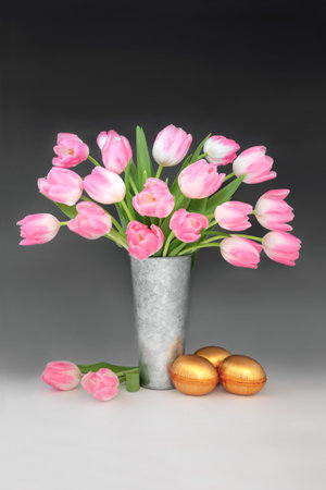 Happy Easter concept with gold eggs  and pink tulip flower arrangement on gradient black white background. Spring floral and festive treats for the holiday season.の写真素材