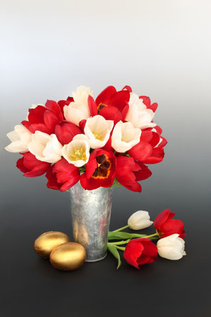 Gold chocolate Easter eggs and red tulip flowers in a vase on gradient black white background. Spring floral, festive luxury gifts for the holiday season.の写真素材