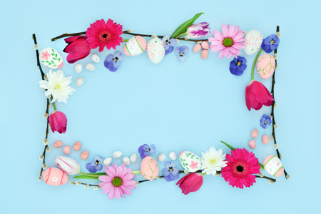 Happy Easter background border with edible and decorative eggs, flowers and willow branches on pastel blue. Flat lay. Natural nature frame design.の写真素材