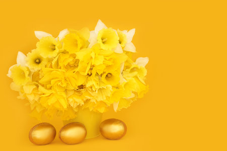 Gold Easter eggs and Spring daffodil flower arrangement on yellow background. Floral luxury seasonal food nature composition.の写真素材