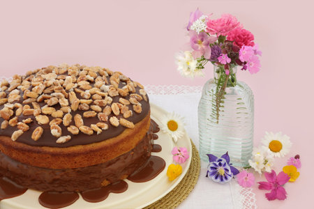 Homemade peanut cake and caramel sauce decorated with peanuts on pink background with summer flowers. Delicious afternoon tea floral composition.の写真素材