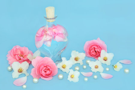 Rosewater for skincare with rose and orange blossom  flowers, heart shaped bottle and pearls on blue. Balances natural skin oils, reduce redness, naturally hydrates skin.の写真素材