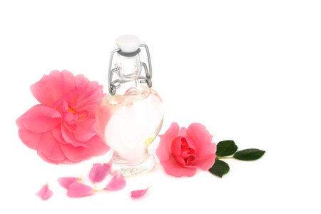 Rosewater for skin care with pink riose flowers on white with heart shaped bottle. Natural product to hydrate skin, treat skin redness, irritation, scars, burns, restore ph balance.の写真素材
