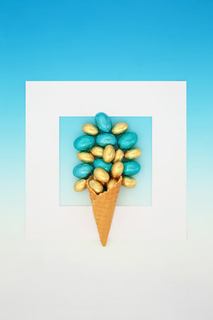 Easter egg ice cream cornet with foil wrapped eggs on gradient blue background, white frame. Surreal abstract design for holiday season.の写真素材