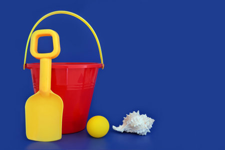 Bucket and spade summer seaside beach toys with conch seashell. Childish holiday symbols in vivid primary colors for travel vacation fun on blue background.の写真素材