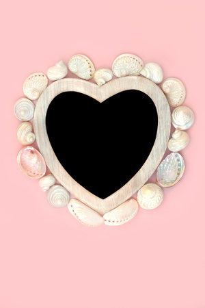 Heart shape mother of pearl seashell wreath with wooden frame on pink background. Romantic symbol for valentines, greeting card, menu, invitationの写真素材