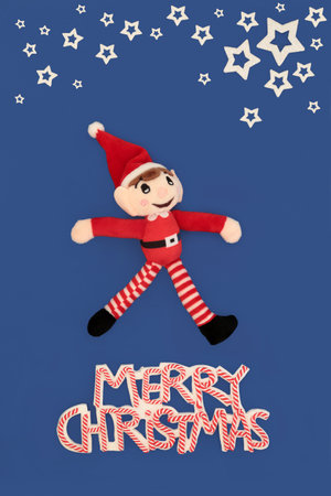 Merry Christmas sign, elf soft toy, white stars on blue backgound. Festive playful whimsical cheerful concept abstract design for holiday season. Xmas card, gift tag. Phrase.の写真素材