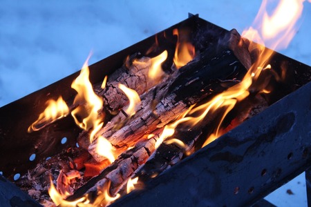 Background of fire and black wood. Dark grey, black white coals on bright fire inside metal brazier. Wood burning in the brazier. Flames fire. Preparation for cooking barbecue.の写真素材
