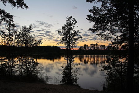 Silhouettes of trees and colorful sky are reflected in the forest lake in the evening. Fantastic landscape. Unusual and picturesque scene. Beauty world. Russia.の写真素材
