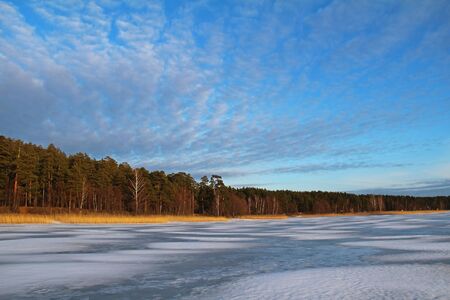 Christmas background with winter forest. Winter landscape with trees, beautiful frozen lake and bushes at sunset. Colorful sky.の写真素材