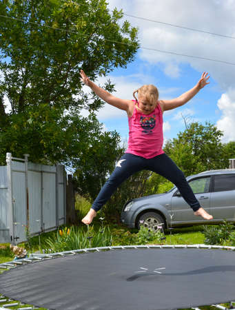 A girl jumps on a trampoline outside in beautiful sunny weather.