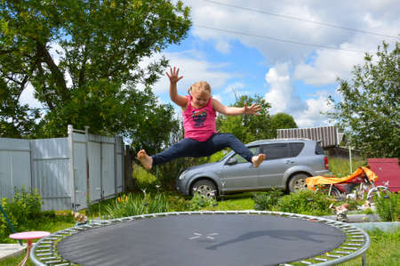 A girl jumps on a trampoline outside in beautiful sunny weather.の写真素材