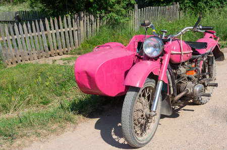 A pink Ural motorcycle with a sidecar stands near the road on a Sunny summer day.
