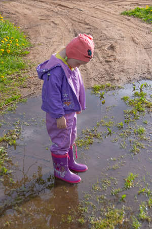 A girl on the street is standing in a puddle and is happy.