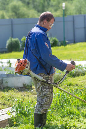 In the village, a young man mows the grass with a petrol mower.
