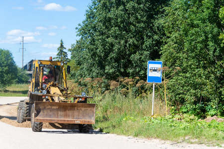 The grader levels a dirt road in a rural area with a special blade with a knife, which is mounted on...