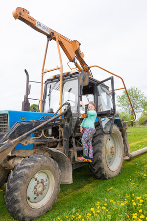 A girl stands on the running board of a tractor.の写真素材