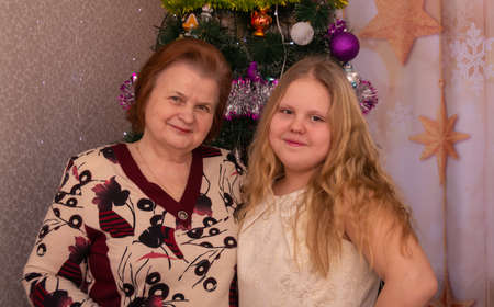 Joyful grandmother and granddaughter near the Christmas tree on New Year's holidays.