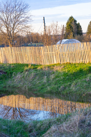 Wooden fence with reflection in a canal in the countryside in winterの写真素材