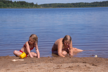 Two girls playing in the water on the shore of the lake.の写真素材