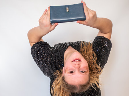 A beautiful model girl in a fashionable black dress holds a leather purse in her hands. Teenager....
