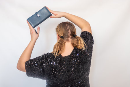 A beautiful model girl in a fashionable black dress holds a leather purse in her hands. Teenager....