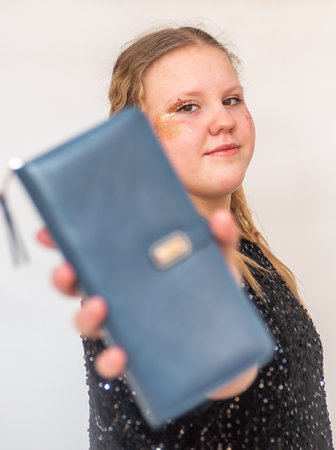 A beautiful model girl in a fashionable black dress holds a leather purse in her hands. Portrait.