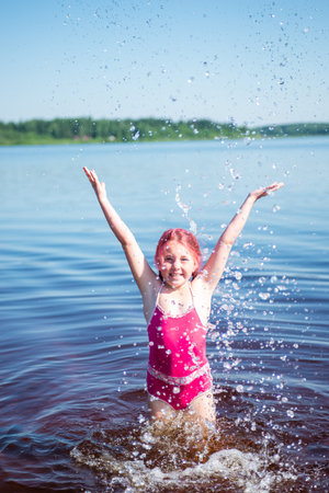 A girl with pink hair is standing in a lake on a hot summer day.の写真素材