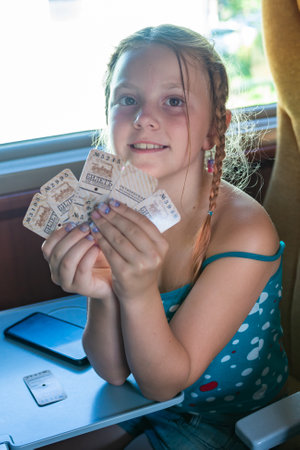 The girl is sitting in the carriage of the retro train and holding vintage train tickets in her hands.の写真素材