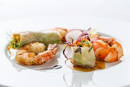 prepared shrimps, spring rolls and salad on white plate