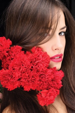 Pretty woman with hair over her right eye and red carnations on her shoulderの写真素材