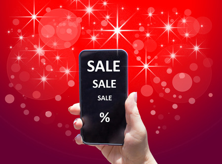The phone with text SALE in female hand on the red background. Concept of Holiday Saleの写真素材