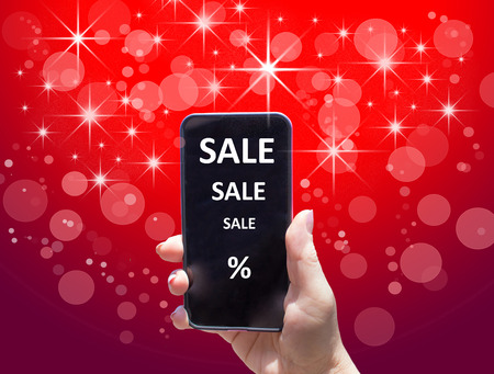 The phone with text SALE in female hand on the red background. Concept of Holiday Saleの写真素材