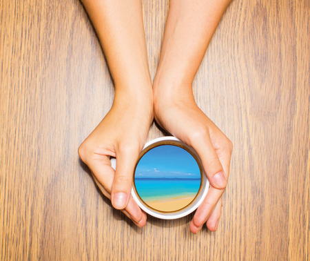 Woman holding cup with dream about tropical vacation against wooden table. Top view. Conceptual photo. Collageの写真素材