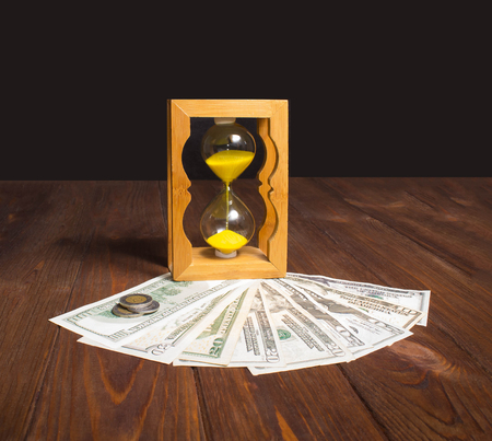 The glossy old-style hourglass standing with american dollar bills