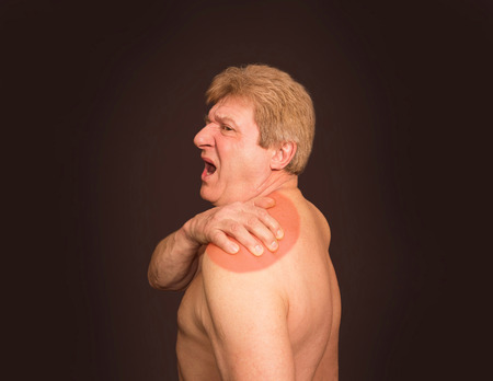 Close-up of senior shirtless man with shoulder pain over black backgroundの写真素材