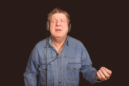 Excited old man listening to music with headphones on dark backgroundの写真素材