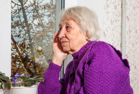 Old lonely woman sitting near the window in his house.の写真素材