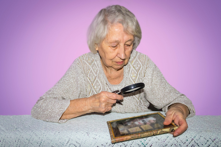 portrait of senior woman looking through a magnifying glass over lilac backgroundの写真素材