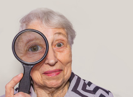 portrait of senior woman looking through a magnifying glass over white backgroundの写真素材