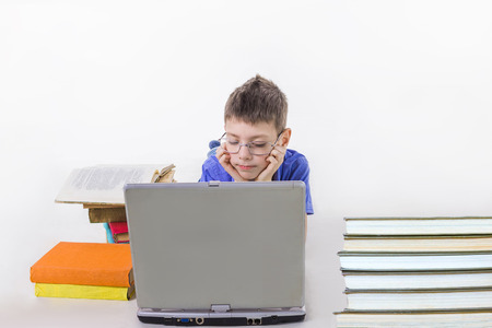 Portrait of cute schoolboy sitting with books and typing on laptop keyboard