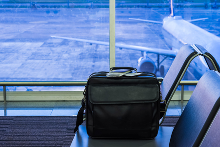 Suitcase in airport departure lounge, airplane in background, summer vacation concept, traveler bag in airport terminal waiting area, empty hall interior with large windowの写真素材