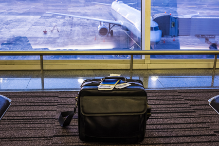Suitcase in airport departure lounge, airplane in background, summer vacation concept, traveler bag in airport terminal waiting area, empty hall interior with large windowの写真素材