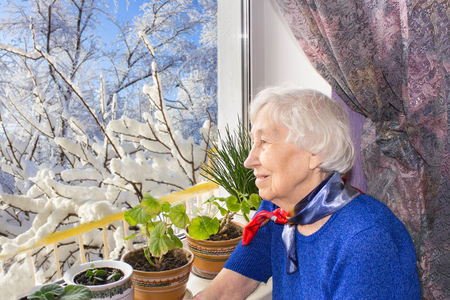 Old lonely woman sitting near the window in his house and looking at camera.の写真素材