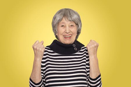 The portrait of a cheerful smiling senior woman gesturing victory over studio backgroundの写真素材