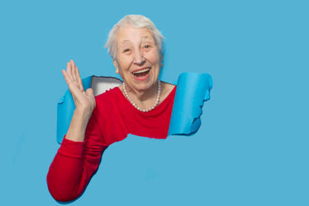 Surprised senior woman looking through hole in paper wall. Shocked lady looks through ripped paper....