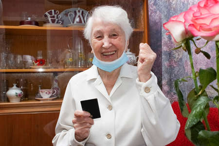 Happy senior woman with face mask making reservation online from home and paying with credit card....