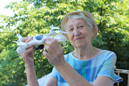 Quadcopter drone in hand of senior woman at balcony. Old people and gadget conceptの写真素材