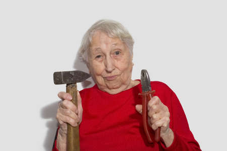 Funny portrait of senior woman holding hammer and pliers in his hand isolated on white studio background.の写真素材