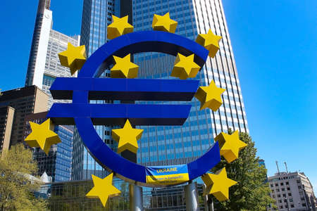 Frankfurt, Germany - December 29, 2022: Euro sign sculpture in a park among modern office towers in...